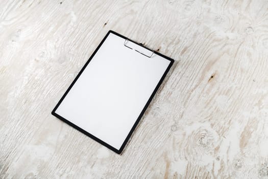 Photo of clipboard with a blank sheet of paper on light wooden background with plenty of copy space. Blank template for design presentations and portfolios. Mock-up for branding identity.