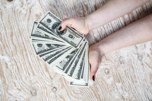 Dollar banknotes in hands. Woman hands counting dollar banknotes on light wooden background.
