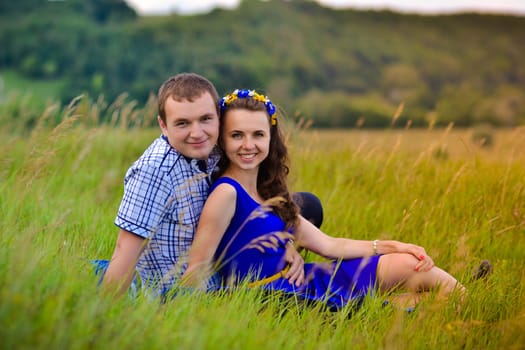 Cheerful,beautiful,smiling happy couple,young family on date.Happy,young couple watching sunset on green sunny meadow.Happy,cheerful,smiling young family has lovely date outdoors.Beautiful couple has good time,sit on green hills with nice view,sun.