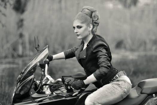 Biker girl.Black and white photo.Professional biker girl,fast rider,sitting on black,fast,modern motorbike,motorcycle,bike.Sexy biker girl with creative,fashionable hairstyle,leather,black jacket riding ahead.Portrait of a girl on bike,new motorbike.