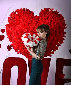 Valentine's day holiday.Cheerful,attractive,beautiful,awesome,lovely girl,woman with a big,large bouquet of white and red roses on the background of big,red heart of many flowers,red roses.Valentine.