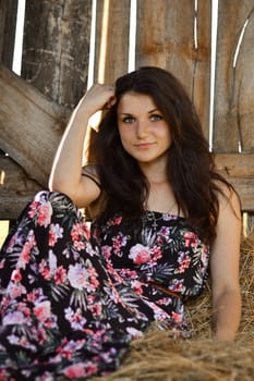 Beautiful girl sitting in the hay.Attractive girl with hay.Gorgeous woman,girl in the wooden stable,stable,yellow,dry stack of hay,haystack.Beautiful girl with lovely,long dress and haystack,hay.Hay.Happy,cheerful,smiling girl with cute nice smile.