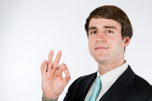 Head-and-shoulder view of a young man around dark suit against a white background showing the O.K. sign and smiling friendly into the camera.
