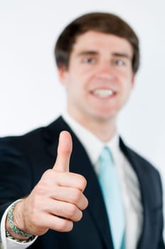 Head-and-shoulder view of a young man around dark suit pointing his thumbs up. Thumb sharply pictured  Body in the blurred background.
