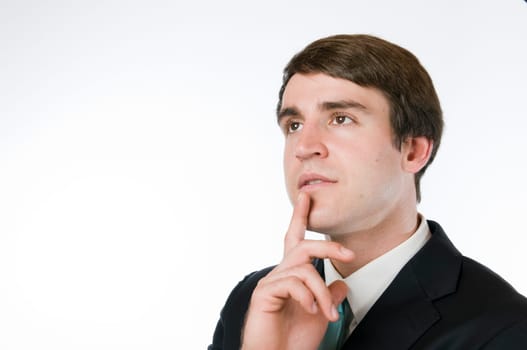 Head-and-shoulder view of a young man around dark suit against a white background,the index finger placed on the chin with a thoughtful look to the top left.