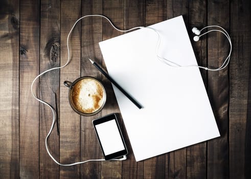 Photo of blank stationery on vintage wooden table background. ID template. Mockup for branding identity. Letterhead, coffee cup, phone, pencil and headphones. Blank objects for placing your design.