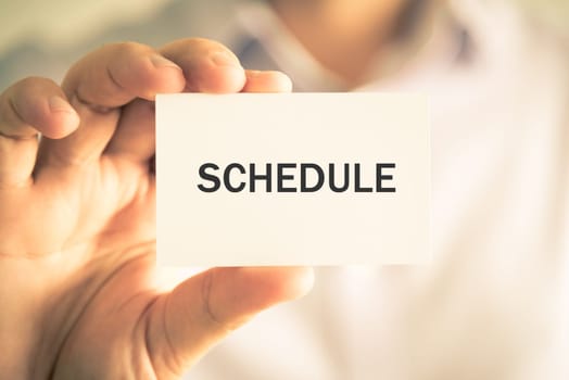 Closeup on businessman holding a card with text SCHEDULE, business concept image with soft focus background and vintage tone