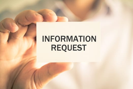 Closeup on businessman holding a card with text INFORMATION REQUEST, business concept image with soft focus background and vintage tone