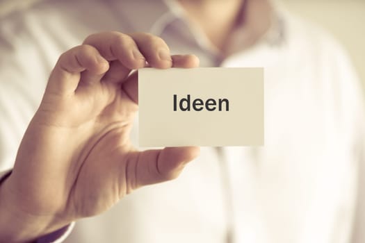 Closeup on businessman holding message card "IDEEN"" written in German - translation : IDEA, business concept image with soft focus background and vintage tone"