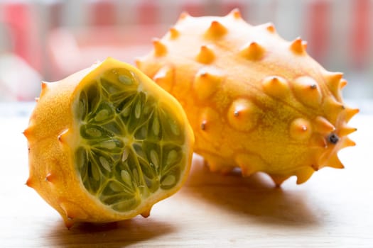 Whole and cut kiwano fruit on cutting board.