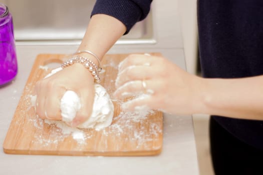 female hands in flour closeup kneading dough on table