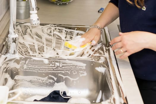 a woman doing chores in kitchen at home, cleaning sink and faucet