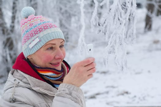 Portrait of an adult woman photographing on mobile phone in winter park