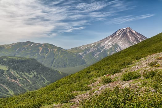 Mountains and volcanoes. Beautiful landscape of Kamchatka Peninsula: summer panoramic view of Mountain Range Vachkazhets, mountain lake and clouds in blue sky on sunny day. Eurasia, Russian Far East, Kamchatka Region.