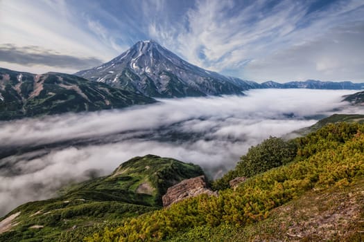 Mountains and volcanoes. Beautiful landscape of Kamchatka Peninsula: summer panoramic view of Mountain Range Vachkazhets, mountain lake and clouds in blue sky on sunny day. Eurasia, Russian Far East, Kamchatka Region.