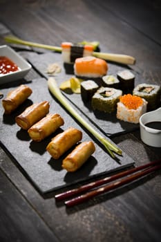 Spring rolls and sushi on black wooden table