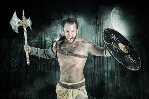 Ancient warrior or Gladiator posing in a dark forest with an axe