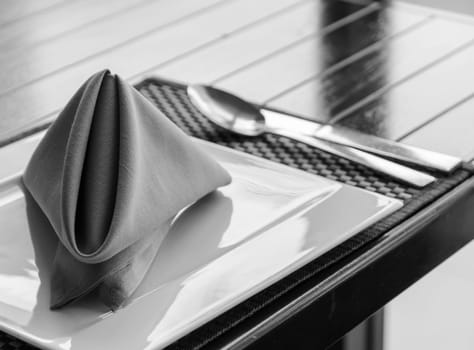 Folded napkin on white plate, table setting in black and white image