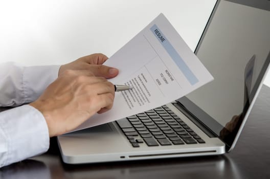 Businessman or job seeker review his resume on his desk with pen and computer laptop.