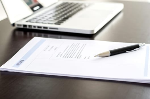 Close-up of resume, pen and computer laptop on black wooden desk. Business or job seeker concept.