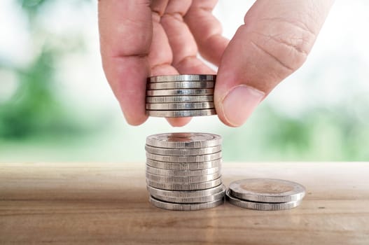 Saving money concept. hand putting coin to stacks of coins on wooden table.