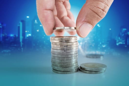 Saving money concept. hand putting coin to stacks of coins with city scape background.