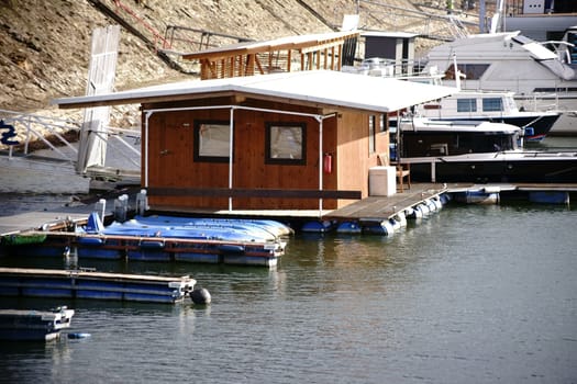 A small wooden houseboat as well as yachts and motor boats anchor in an inland port on the river Rhine.