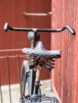 old retro antique black men's bicycle parked up of red wooden fence photographed from behind