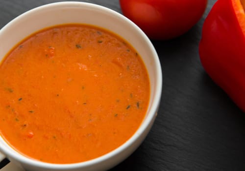cream soup with roasted peppers and tomatoes on black plate