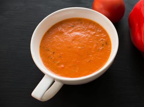 cream soup with roasted peppers and tomatoes on black plate