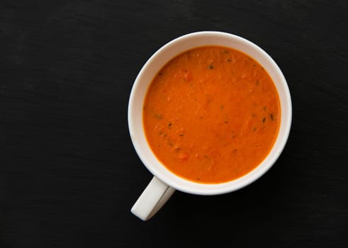 cream soup with roasted peppers and tomatoes on black plate,top view