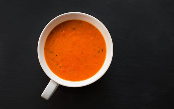 cream soup with roasted peppers and tomatoes on black plate,top view