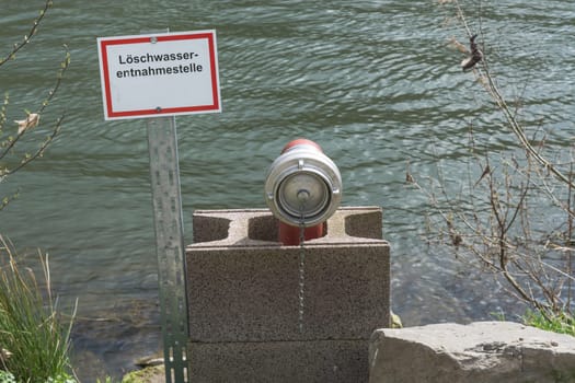 Sign with inscription in German extinguishing water outlet. Firefighting equipment in a river..