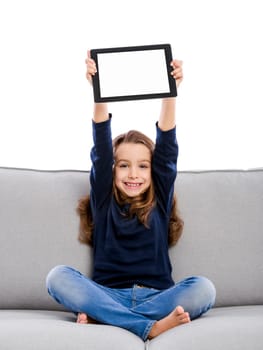 Happy little girl sitting on a couch and working a laptop