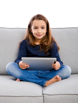 Happy little girl sitting on a couch and working a laptop