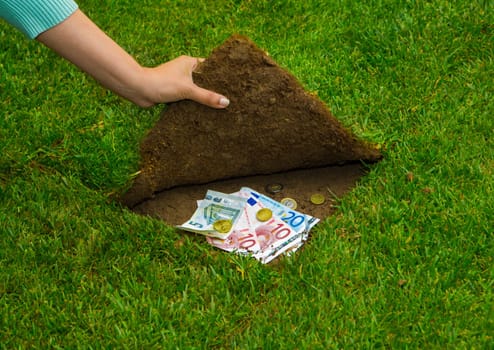 Finances concept, hands hiding money under the grass
