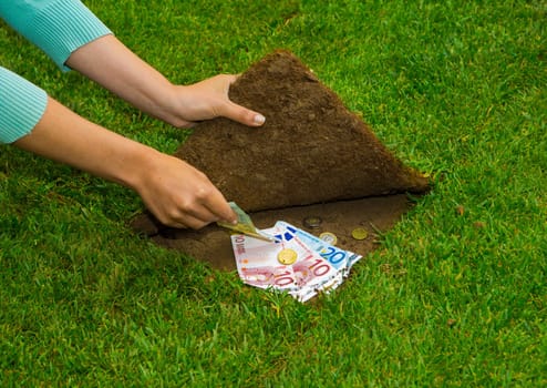 Finances concept, hands hiding money under the grass