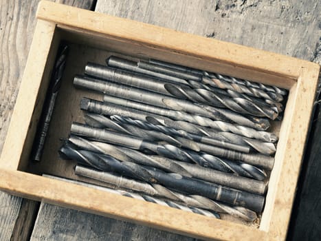 Old used drills in a wooden box on a workbench, top view vintage color toned