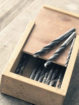 Old used drills in a wooden box on a workbench