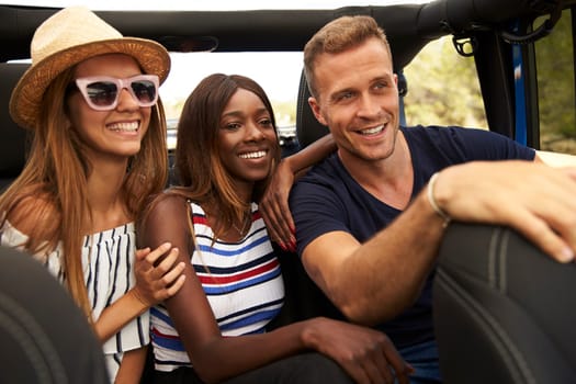 Group Of Friends Driving Open Top Car On Country Road
