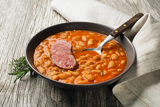 White bean stew with fresh spices and sausage on wooden table