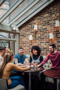 Friends are socialising over coffee in a coffee shop. They are laughing and talking with their drinks in their hands.