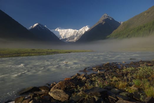 The mountain river in the mountains. Current through the gorge the river. Stones and rocky land near the river. Beautiful mountain landscape.