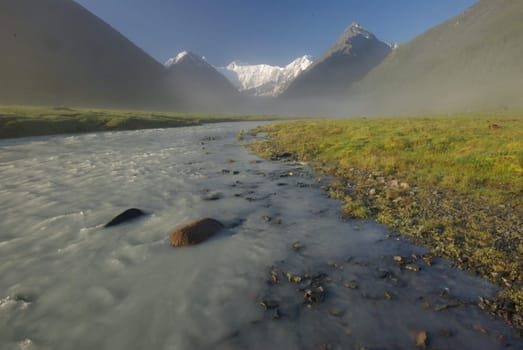 The mountain river in the mountains. Current through the gorge the river. Stones and rocky land near the river. Beautiful mountain landscape.