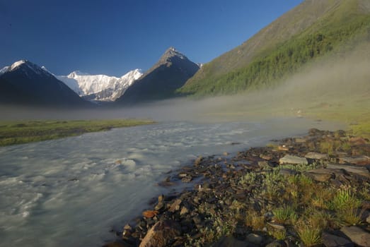 The mountain river in the mountains. Current through the gorge the river. Stones and rocky land near the river. Beautiful mountain landscape.