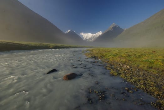 The mountain river in the mountains. Current through the gorge the river. Stones and rocky land near the river. Beautiful mountain landscape.