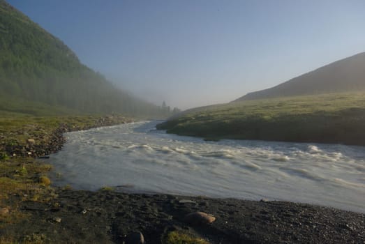 The mountain river in the mountains. Current through the gorge the river. Stones and rocky land near the river. Beautiful mountain landscape.