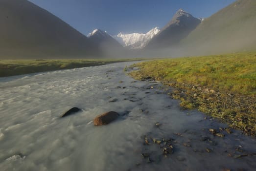 The mountain river in the mountains. Current through the gorge the river. Stones and rocky land near the river. Beautiful mountain landscape.