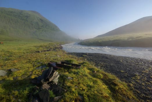 The mountain river in the mountains. Current through the gorge the river. Stones and rocky land near the river. Beautiful mountain landscape.
