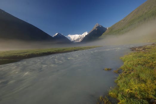 The mountain river in the mountains. Current through the gorge the river. Stones and rocky land near the river. Beautiful mountain landscape.